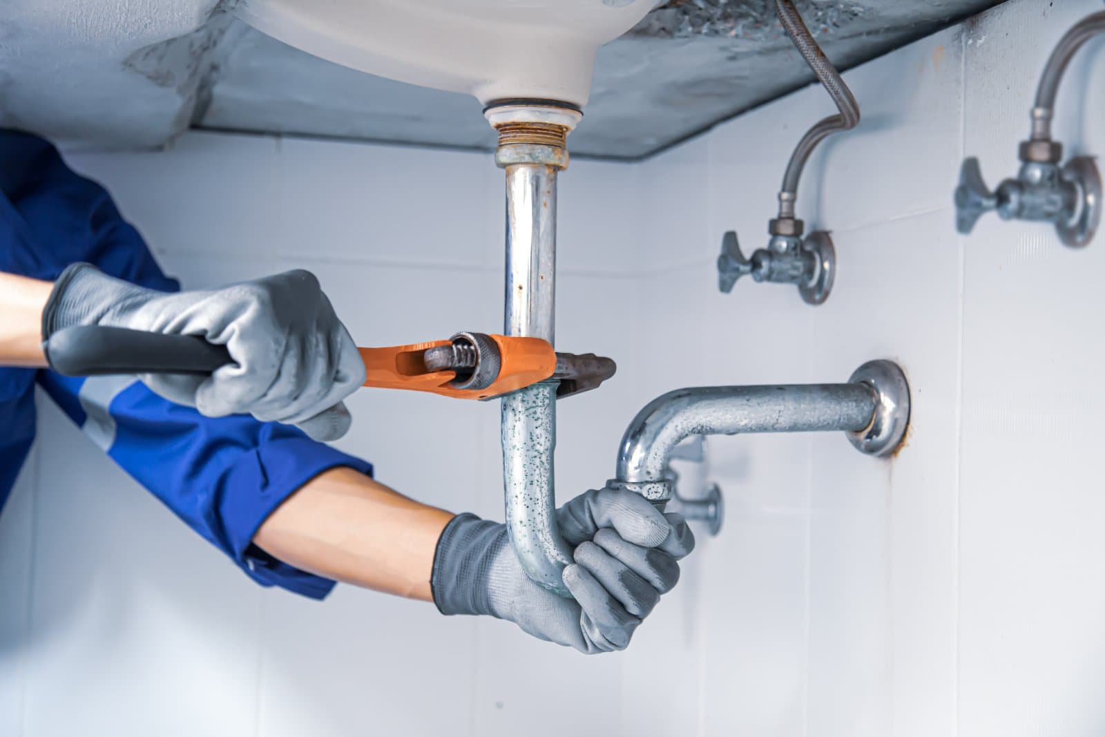 Gloved hands with a wrench on the pipework under a sink